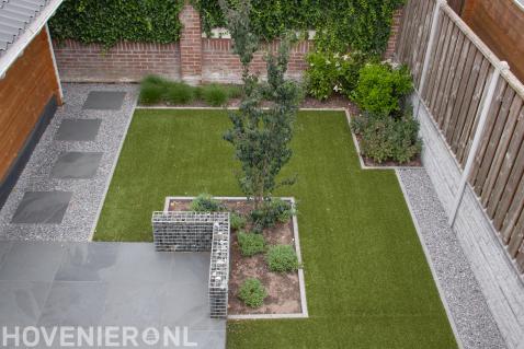 Moderne tuin met bestrating van grote tegels, schanskorf en kunstgras