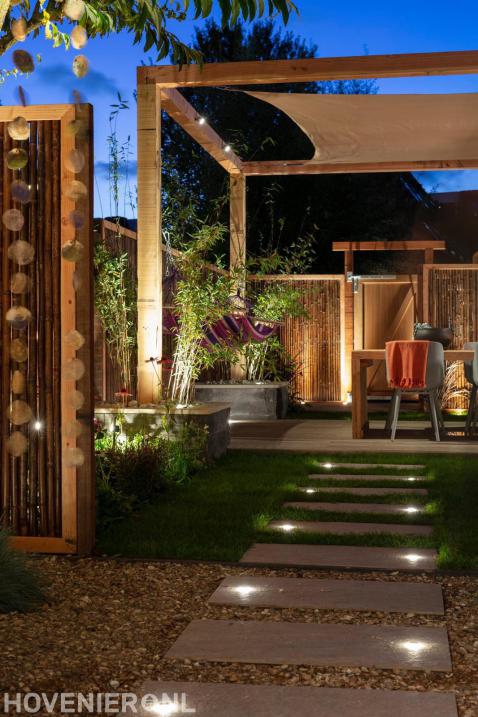 Sfeervolle buitenverlichting in tuin met pergola en bamboe schutting