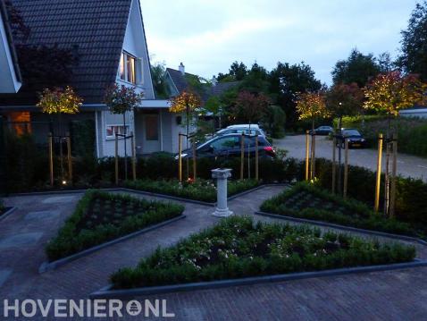 Voortuin met bestrating en driehoekige borders omgeven met buxus