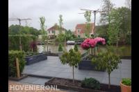 Strakke tuin aan het water met siertegels, plantenbakken en leibomen