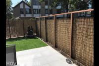 Tuinaanleg met bestrating, kunstgras en schutting met bamboematten