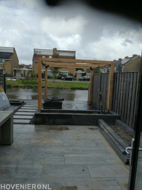 Tuin aan het water met bestrating, plantenbakken en houten pergola