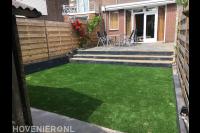 Achtertuin met kunstgras en trap naar verhoogd terras