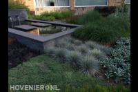 Strakke vijver met watermuur omgeven door siergrassen