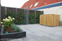 Tuinaanleg met natuursteen tegels, plantenbak en hedera schutting