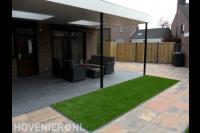 Tuin met terrasoverkapping, kunstgras en bestrating van natuursteen 1