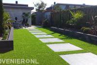 Achtertuin met grote tegels omgeven door kunstgras