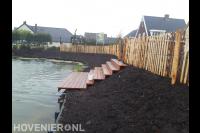 Tuinafscheiding van kastanjehouten palen en vlonder aan het water