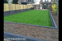 Achtertuin met strak gazon, verhoogde borders en schutting