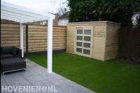 Achtertuin met terrasoverkapping, kunstgras en houten schuurtje