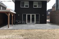 Achtertuin met bestrating van grote siertegels en houten overkapping