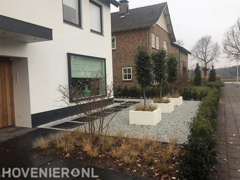 Moderne voortuin met grote tegels, grind en witte plantenbakken 1