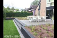 Achtertuin met gazon en stenen trap naar verhoogd terras