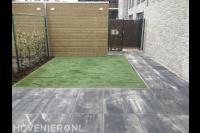 Tuinaanleg met kunstgras, natuursteen tegels en hedera schutting