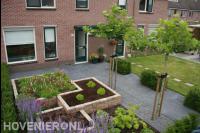 Strakke voortuin met bestrating en nieuwe planten in verhoogde borders