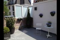 Kleine achtertuin met bestrating van lichte tegels en bloempotten 1