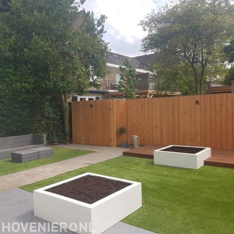 Moderne tuin met kunstgras, houten vlonder en witte bloembakken