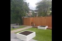 Moderne tuin met kunstgras, houten vlonder en witte bloembakken