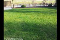 Tuin aan het water met gazon, terras en hekwerk van betongaas