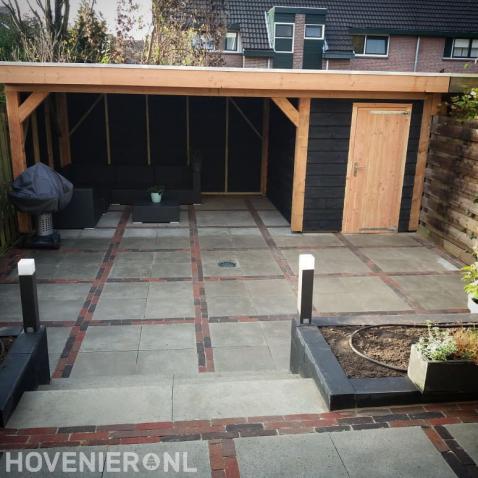 Tuin met sierbestrating, plantenbakken en overkapping met berging