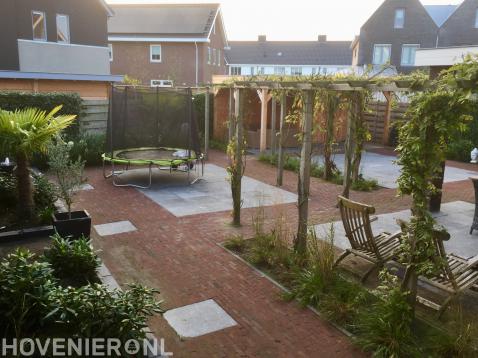 Tuin met bestrating van klinkers en siertegels en houten pergola