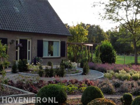 Voortuin met kleurrijke beplanting, buxusbollen en pergola