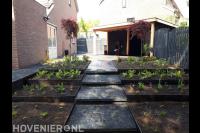 Tuinaanleg met houten overkapping en borders met hoogteverschillen