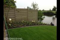 Tuin aan het water met gazon en jonge planten in border