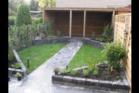 Kleine achtertuin met houten overkapping, gazon en verhoogde borders