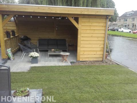 Tuin aan het water met houten overkapping en gazon van graszoden