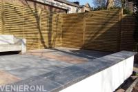 Houten schutting en terras van betontegels en klinkers met houten bank