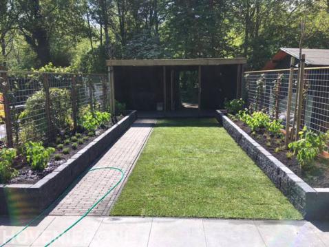Tuin met overkapping, gazon, bloembakken en schutting van betongaas