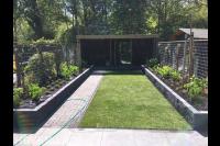 Tuin met overkapping, gazon, bloembakken en schutting van betongaas