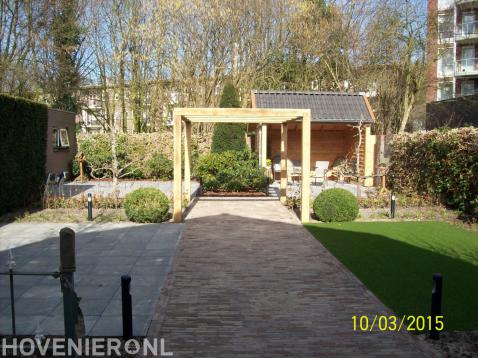 Achtertuin met bestrating, kunstgras, houten pergola en overkapping