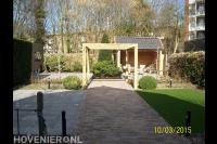 Achtertuin met bestrating, kunstgras, houten pergola en overkapping
