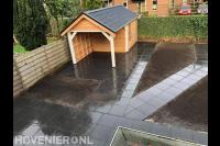 Houten schuurtje met overkapping en straatwerk van betontegels