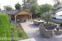 Tuinaanleg met grote siertegels, houten overkapping en beplanting