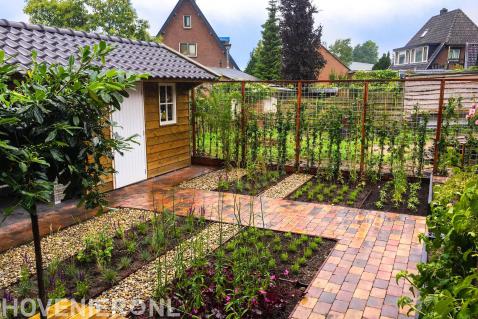 Tuinpad van gekleurde koppelstenen naar houten kapschuur met dakpannen