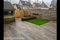 Tuinaanleg met natuursteen tegels, kunstgras en plantenbak