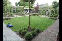 Achtertuin met gazon, houten pergola's en tuinhuisje