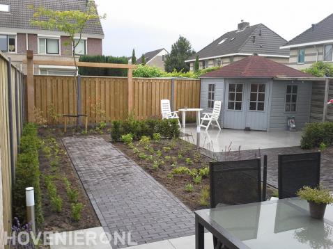 Tuinaanleg met houten schutting en pergola, bestrating en tuinhuis