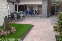 Makkelijke achtertuin met kunstgras en bestrating in wildverband