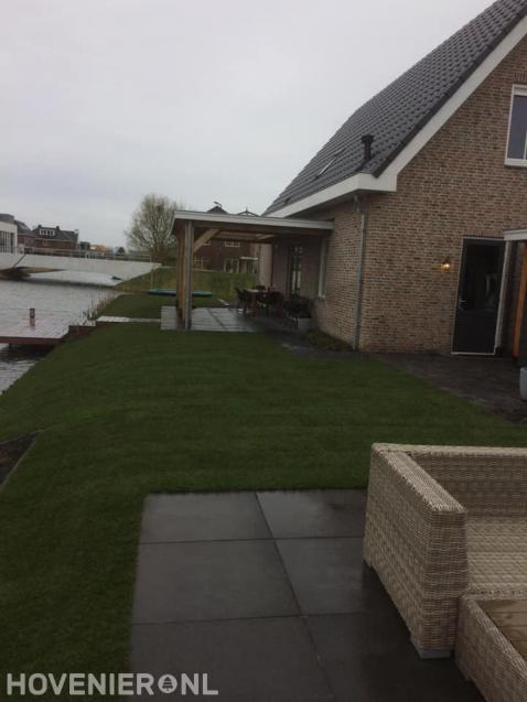 Tuin aan het water met gazon en terras met overkapping