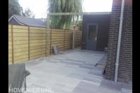 Achtertuin met bestrating van natuursteen tegels en houten schutting