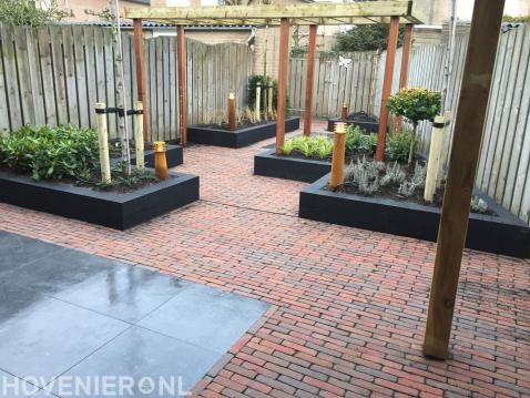 Achtertuin met houten pergola, borders van stapelblokken en waaltjes