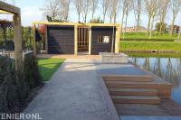 Tuin aan het water met bestrating, gazon en houten schuurtje