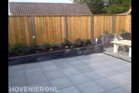 Tuinaanleg met bestrating van natuursteen, plantenbak en schutting