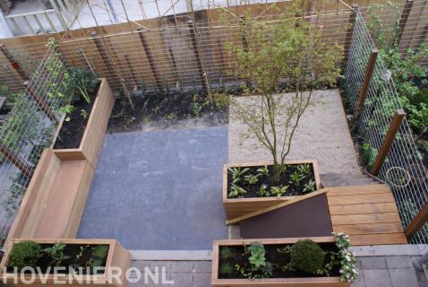 Tuin met houten plantenbakken en bankje en schutting van betongaas
