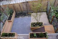 Tuin met houten plantenbakken en bankje en schutting van betongaas