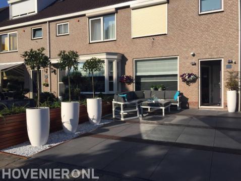 Moderne achtertuin met grote tegels, witte bloempotten en loungeset